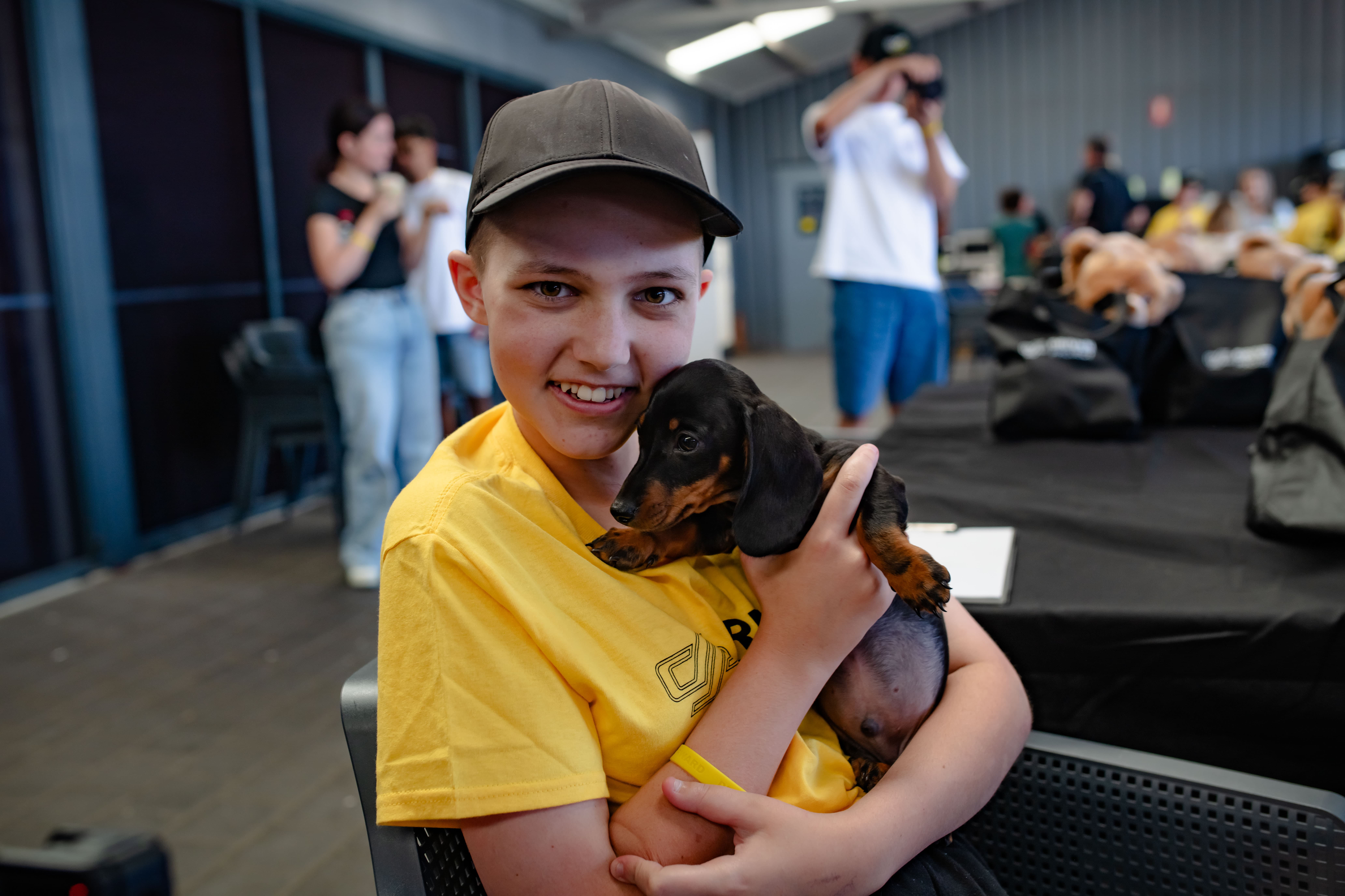 Child in a yellow Driven Project shirt holding a puppy and smiling at the camera