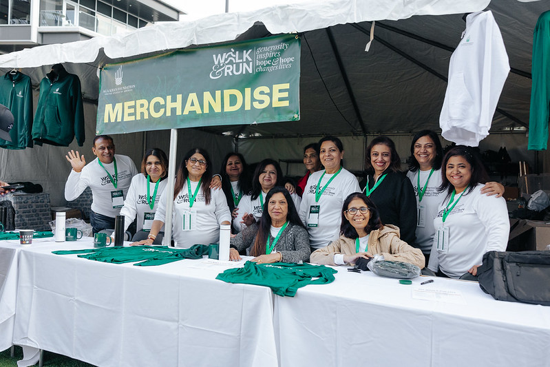 A group of volunteers smile and wave from a merchandise area at the Atlanta Walk & Run A group of volunteers smile and wave from a merchandise area at the Atlanta Walk & Run