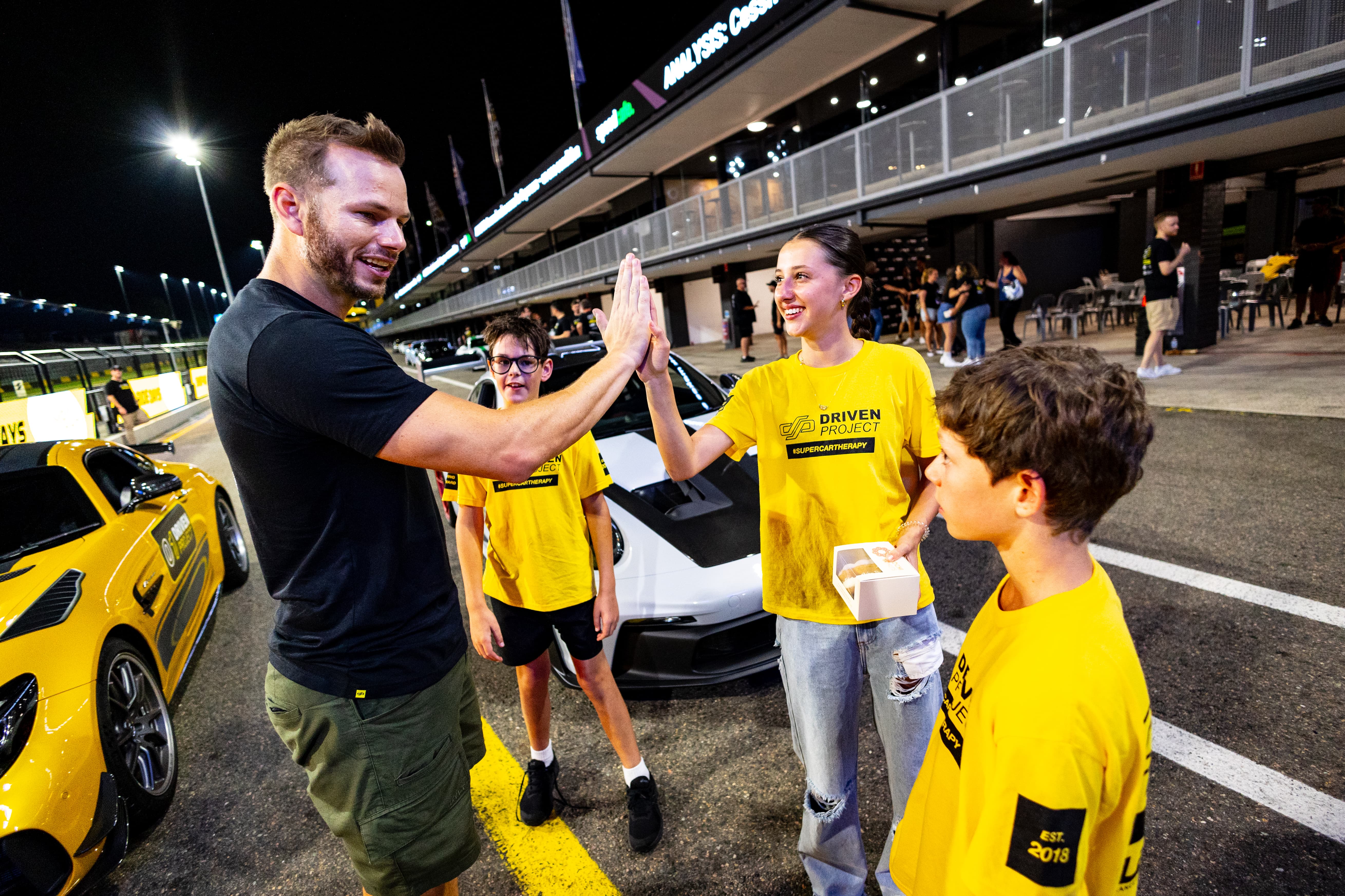 A child wearing a Driven Project shirt hi-fiving a Driven Project team member