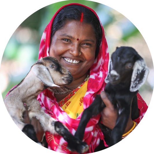 An Indian woman smiles at the camera holding two goats.