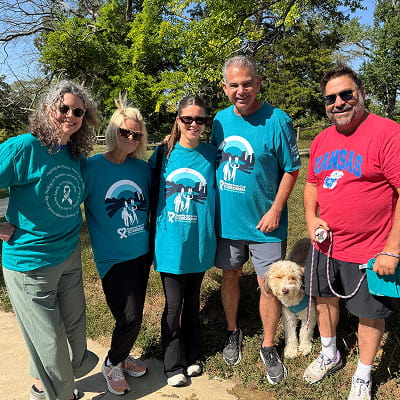 Group of people in teal event shirts posing outdoors with a dog.