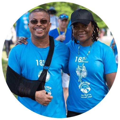Two smiling people in matching blue event shirts pose together outdoors.