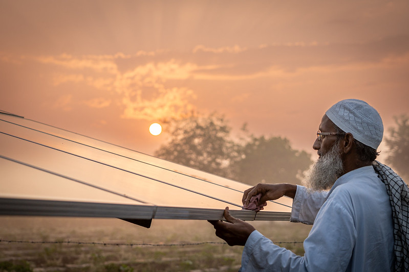 a man examines a solar panel in front of a sunset