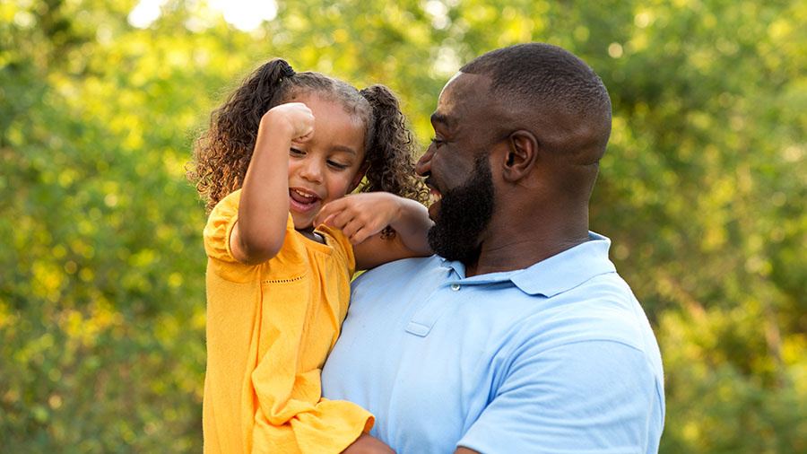 Father holding young daughter who is flexing her muscle