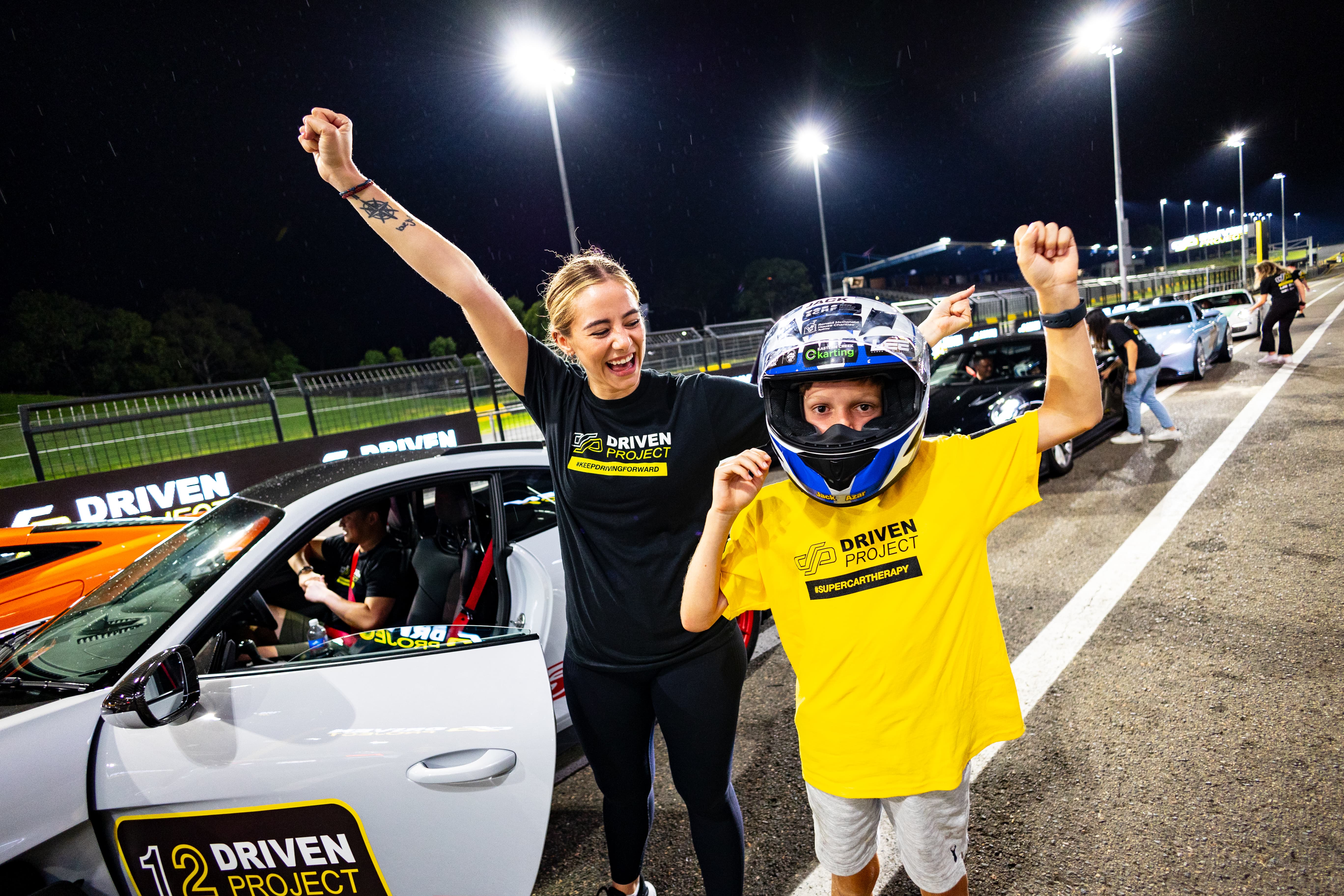 Child and volunteer in Driven Project shirts cheering next to a supercar